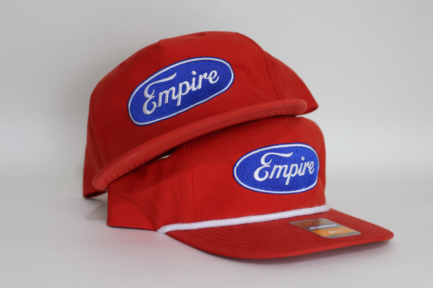 Two red caps with 'Empire' logo on a white background. custom embroidered merch.
