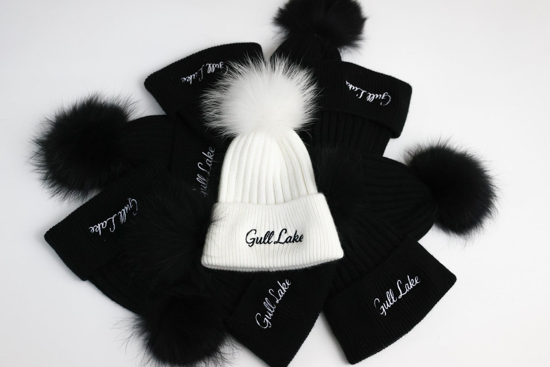 Black beanies with white pom-poms and 'Gull Lake' embroidery on a light gray background