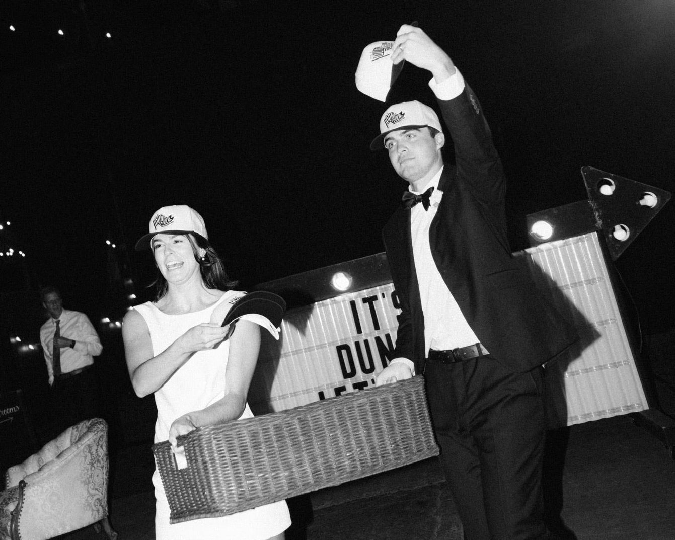 Man and woman in formal attire with a basket on a dance floor at night.